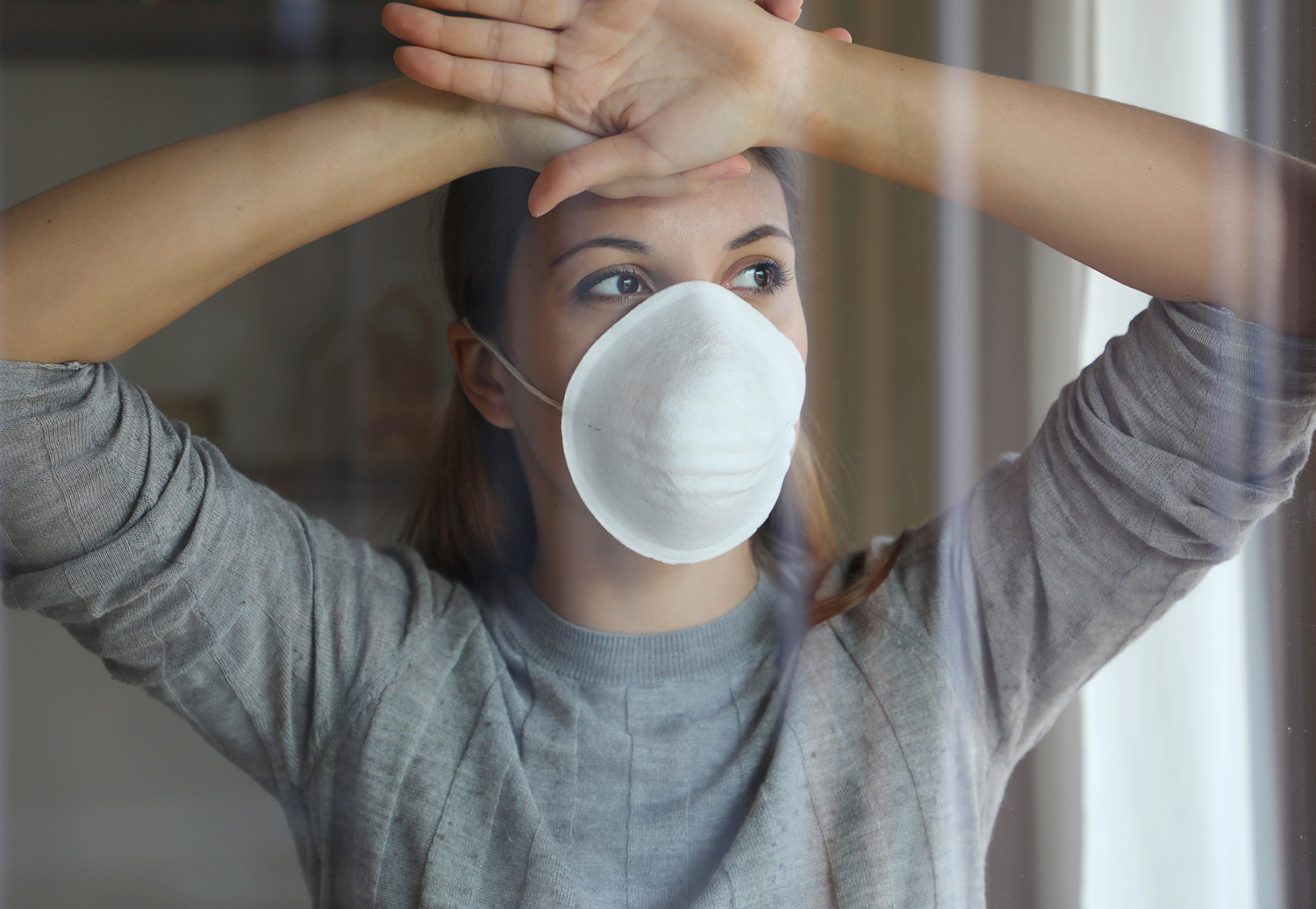 A woman in a face mask looking longingly out of a window.