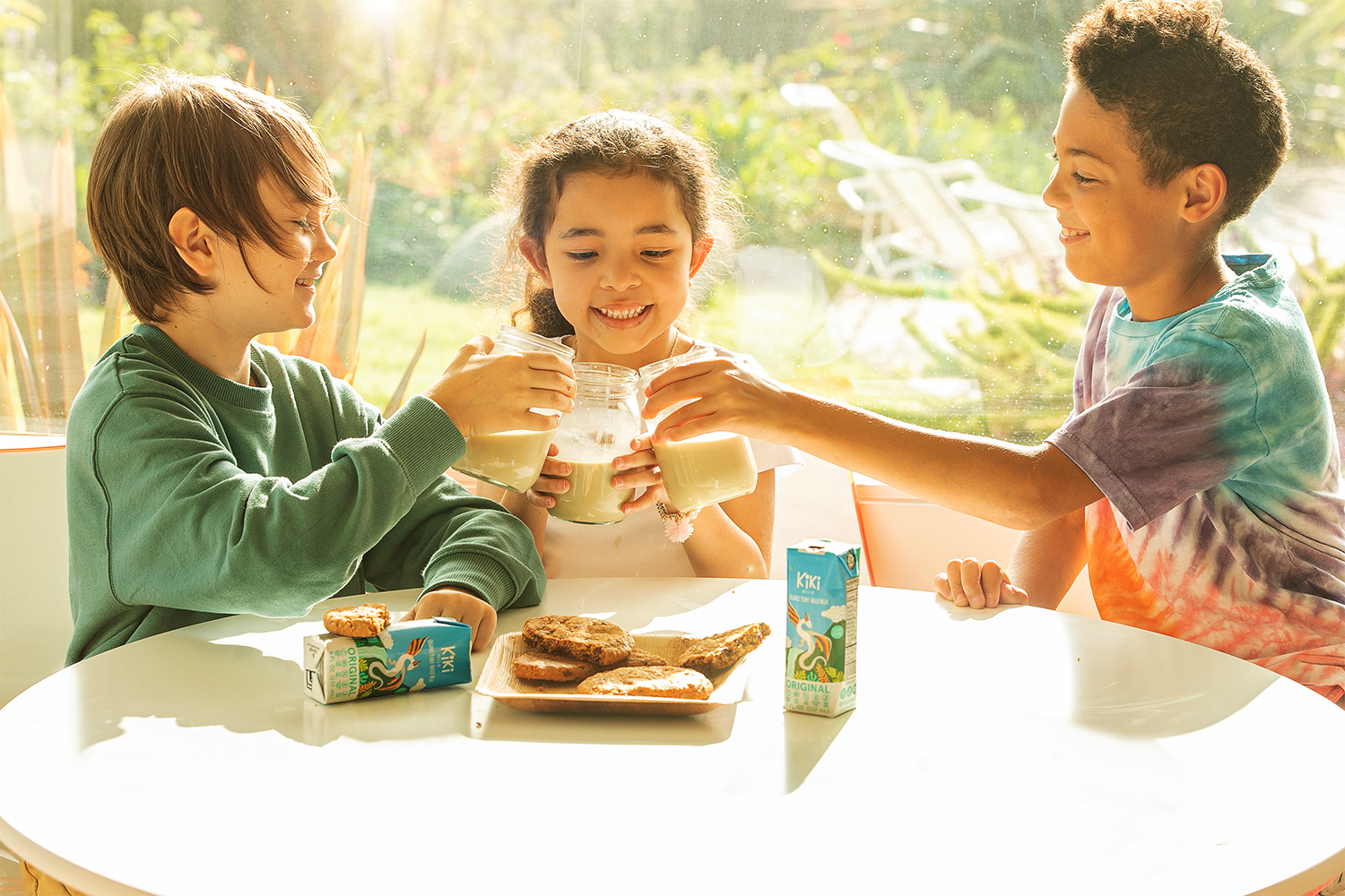 kids sitting around a plate of cookies, cheering with glasses of plant-based milk