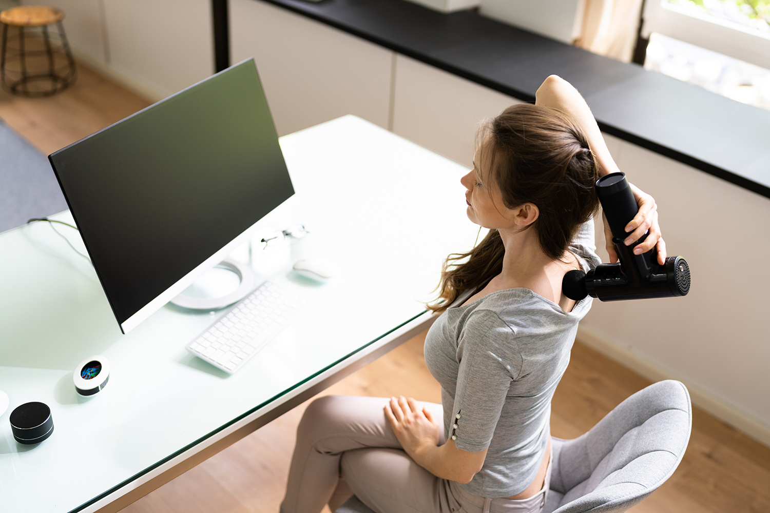 a woman using a massage gun on her neck, her back
