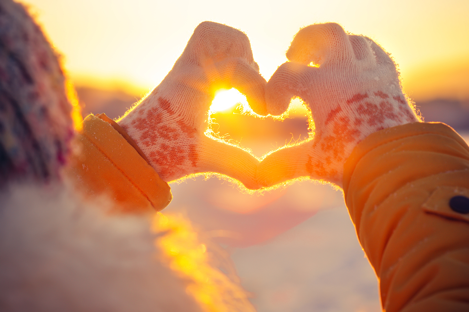 A woman's hands in knitted winter glove making a heart symbol.