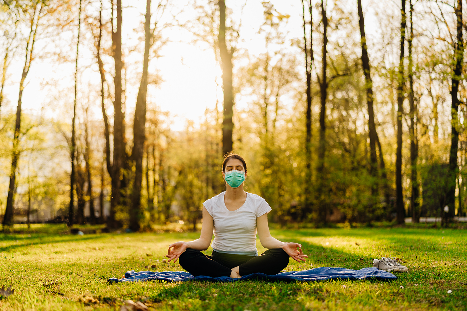 a woman wearing a mask, meditating in a sunny park