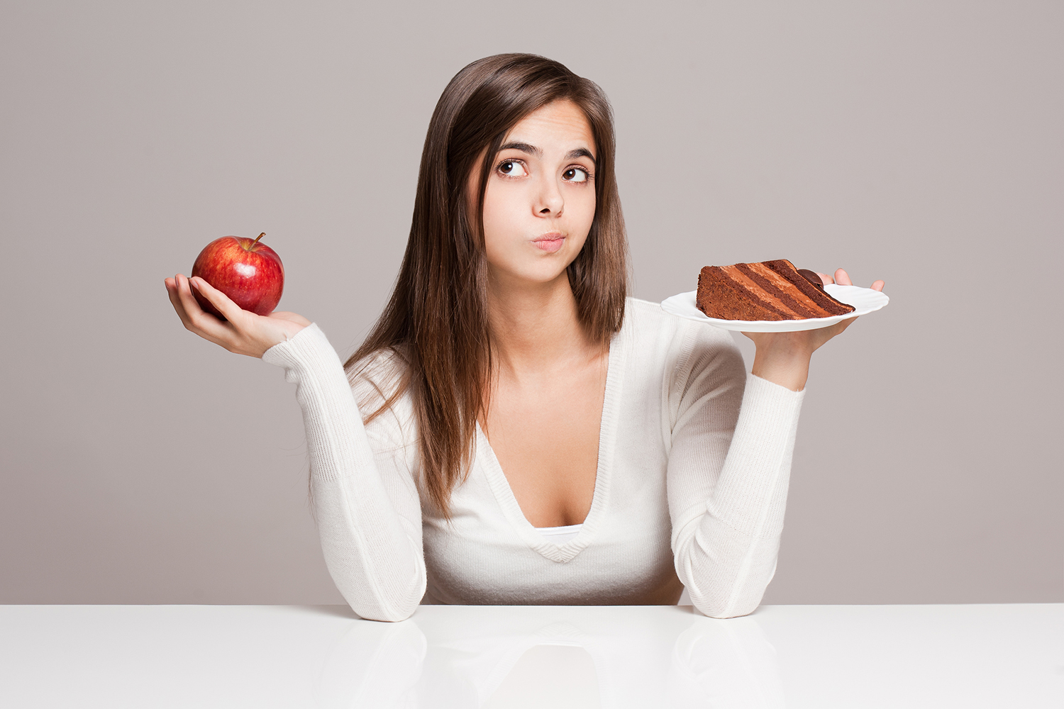 a young woman choosing between an apple and a slice of cake