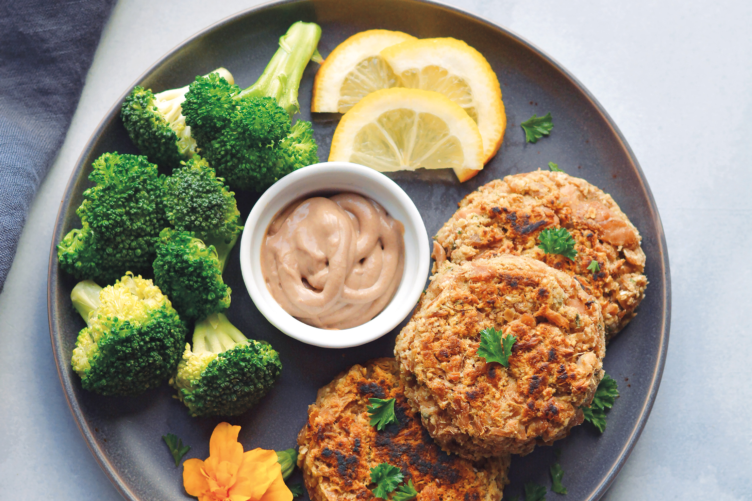 tuna cakes plated with hummus, broccoli, and lemon slices