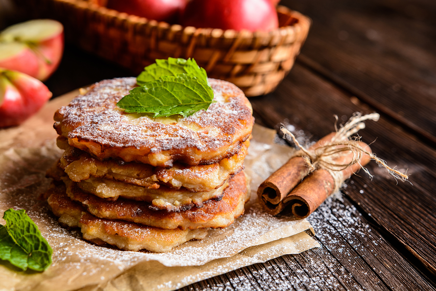 Apple Jack Pancakes stacked on a piece of parchment paper sprinkled with powdered sugar.