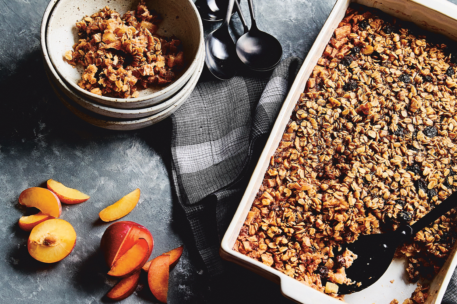 Top view of Baked Apple Maple Oatmeal in a ceramic pan, next to a stack of bowls with a serving of baked oatmeal in the top bowl.