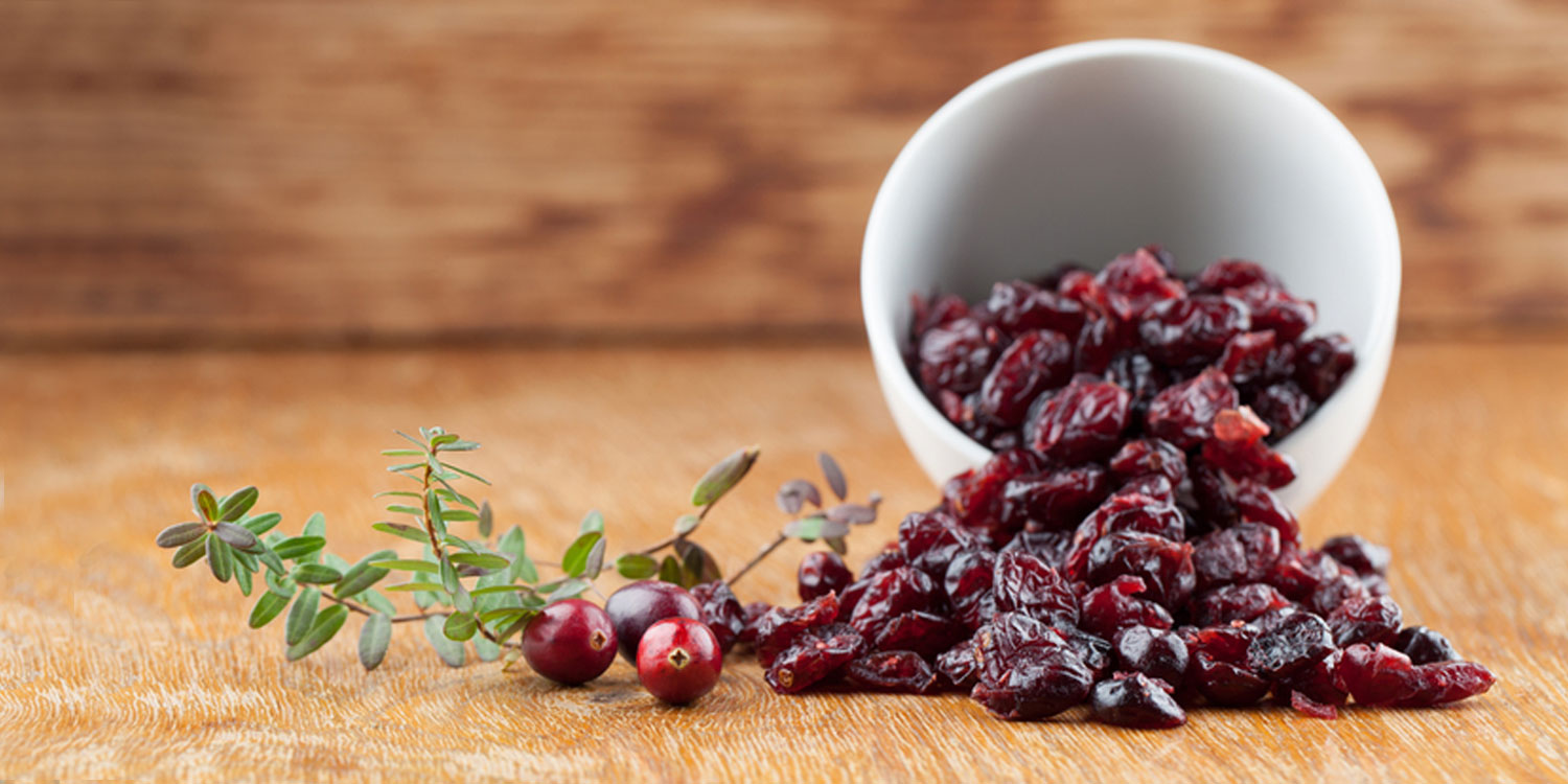Cranberries spilling out of bowl on wooden table