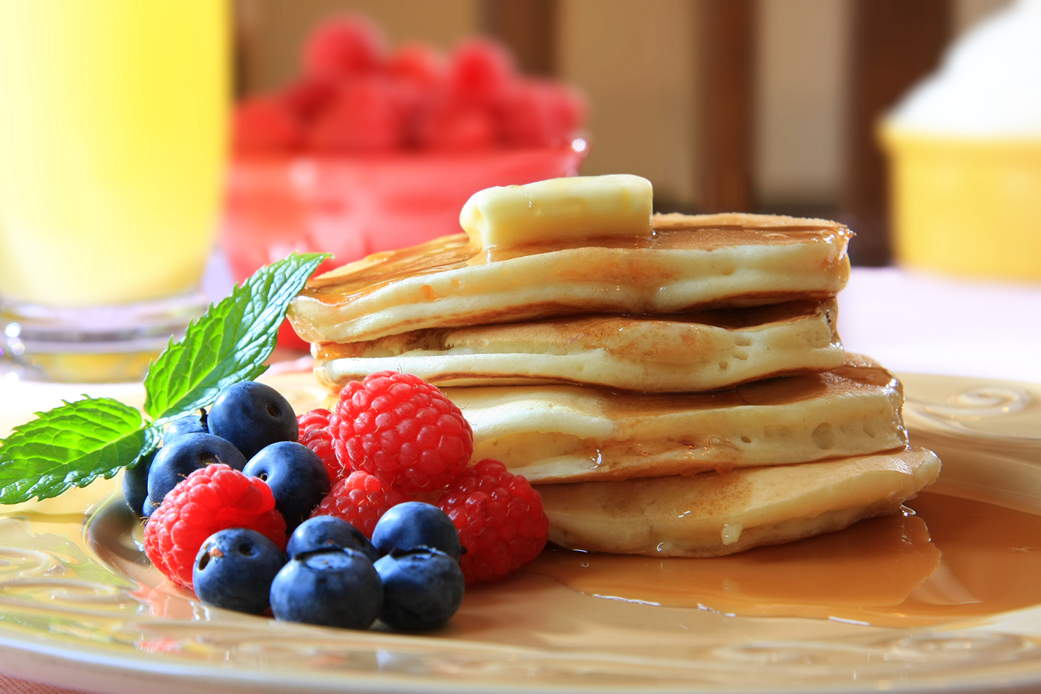 a stack of homemade pancakes from scratch with berries, syrup, and butter