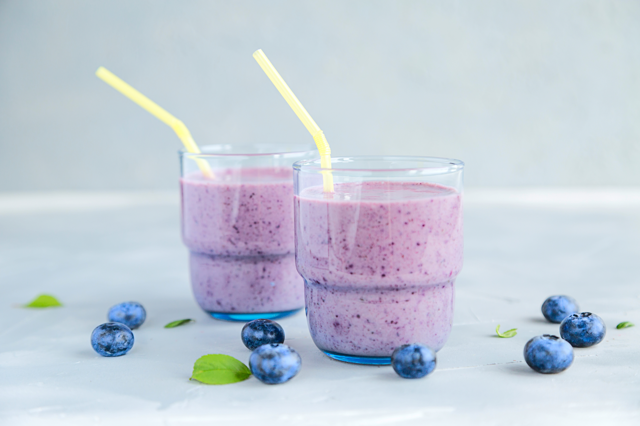 Two glasses of blueberry spinach smoothies, each with a pale yellow straw. 