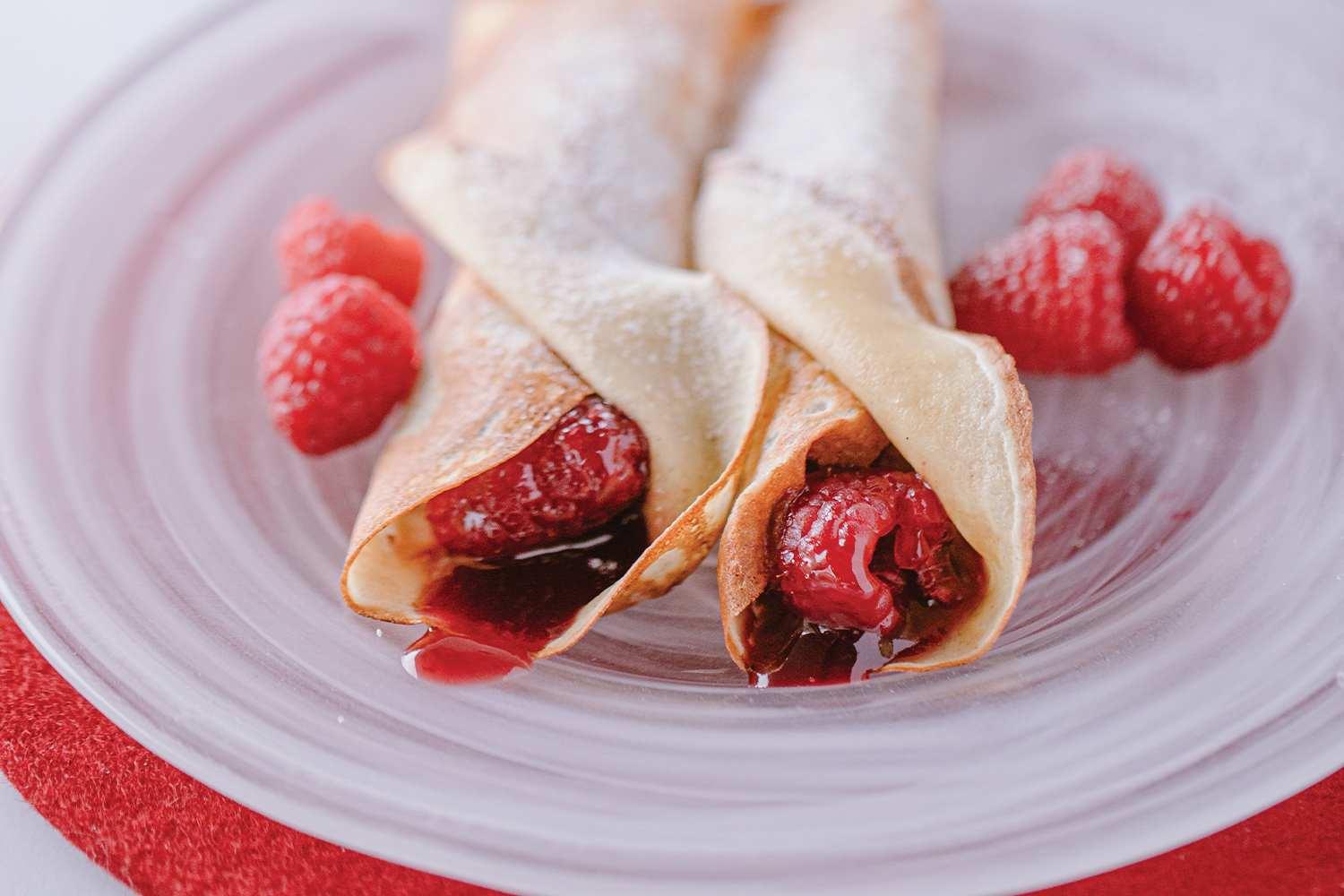 Jam Crêpes with Vanilla Sugar on a white swirled glass plate garnished with raspberries.
