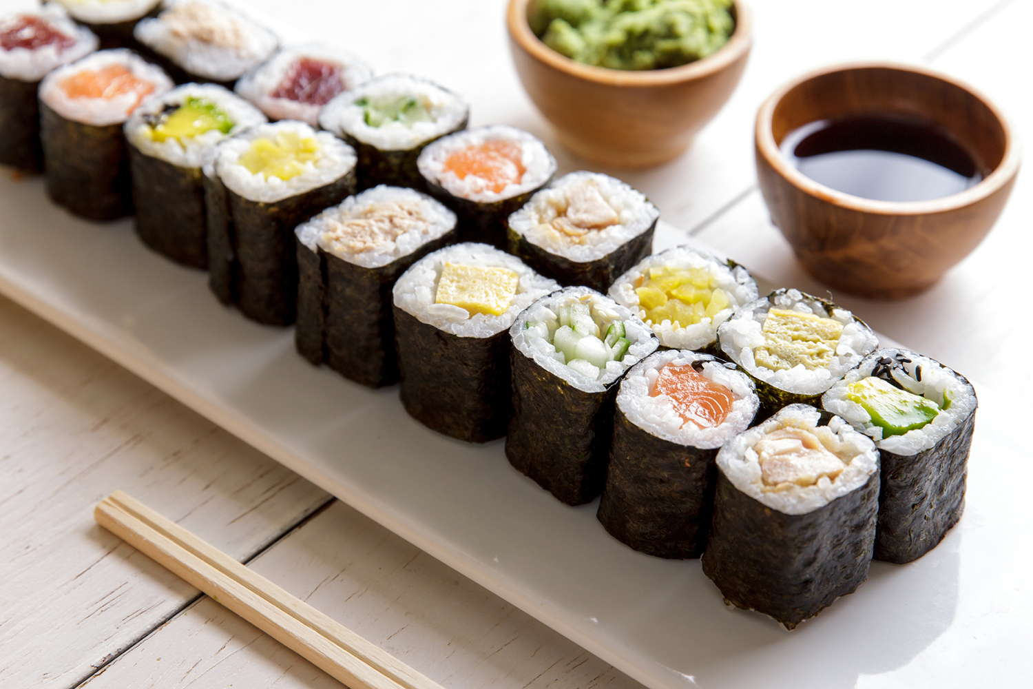 Mini maki sushi platter on white wooden table.
