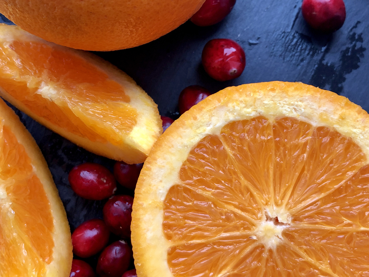 Cranberries and sliced oranges on a dark blue background.