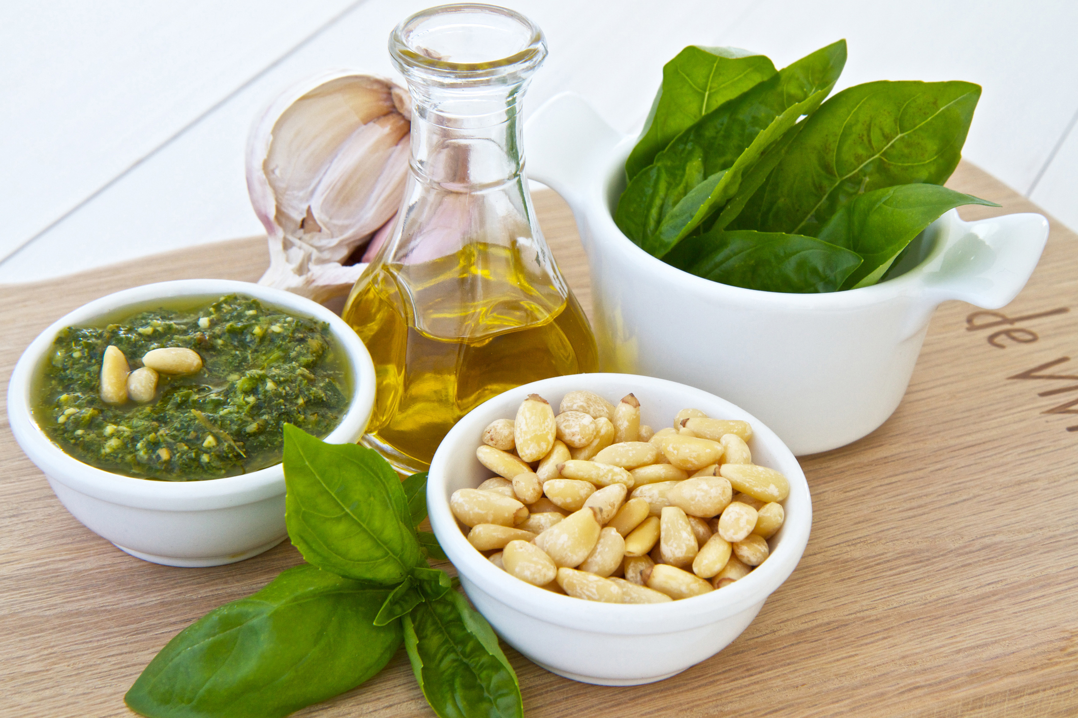 Bowl of pesto with the ingredients displayed on a wood cutting board. 