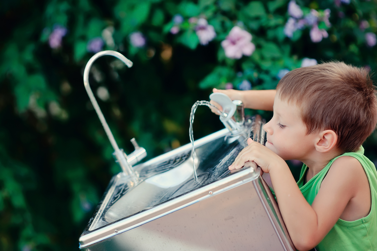 a young boy drinking from a water bubbler fountain in the park