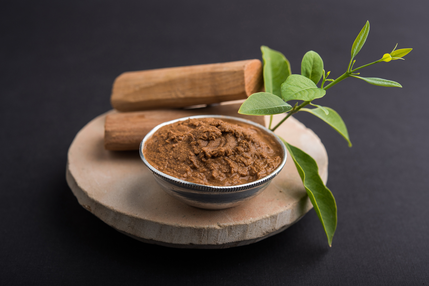 Sandalwood paste in silver bowl with sticks and leaves on a circular stone base for creating paste.