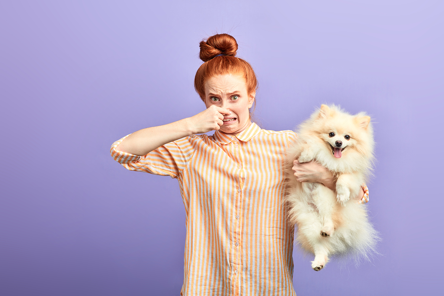 a woman pinching her nose while holding a stinky dog