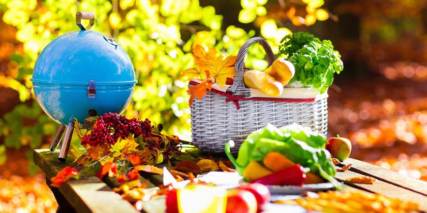 A portable grill and picnic basket on an outdoor table.