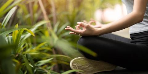 a woman meditating outside, surrounded by plants