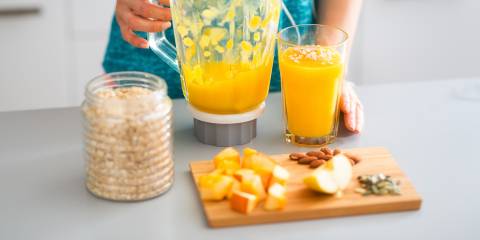 A woman making a protein smoothie with fresh fruits, nuts, and seeds
