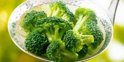 Steamed broccoli in a stainless steel ladle.