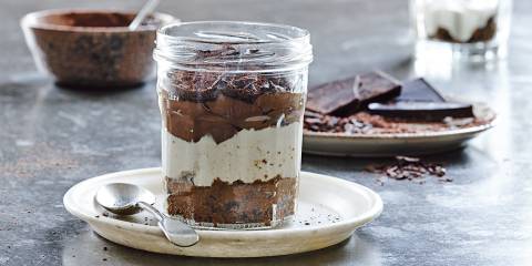 Tiramisu in a clear jar on a white plate with spoon. 