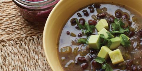 A bowl of black bean soup garnished with lime-pickled red onion and avocado