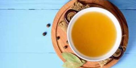 A top view of a pot of Homemade Chicken Broth on a blue background.