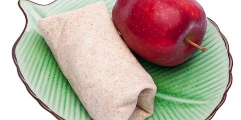 a wrap on a leafy green plate next to an apple
