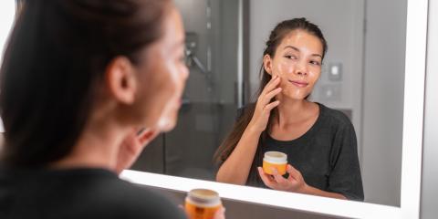 A woman adding honey to her skin in front of a bathroom mirror. 
