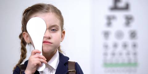a little girl covering one eye during an exam at the optometrist's