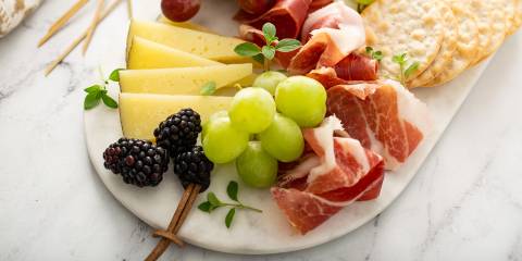 a serving board with fruit, cheese, meat, and crackers