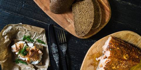 Scandinavian sandwich with smoked salmon fillet on black bread with soft cheese on a black wooden table.