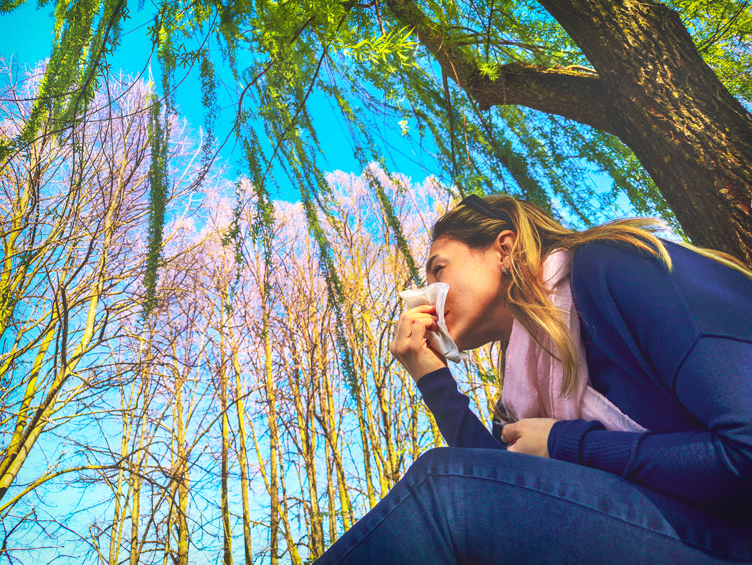 A woman under a willow tree wiping her nose with a tissue.
